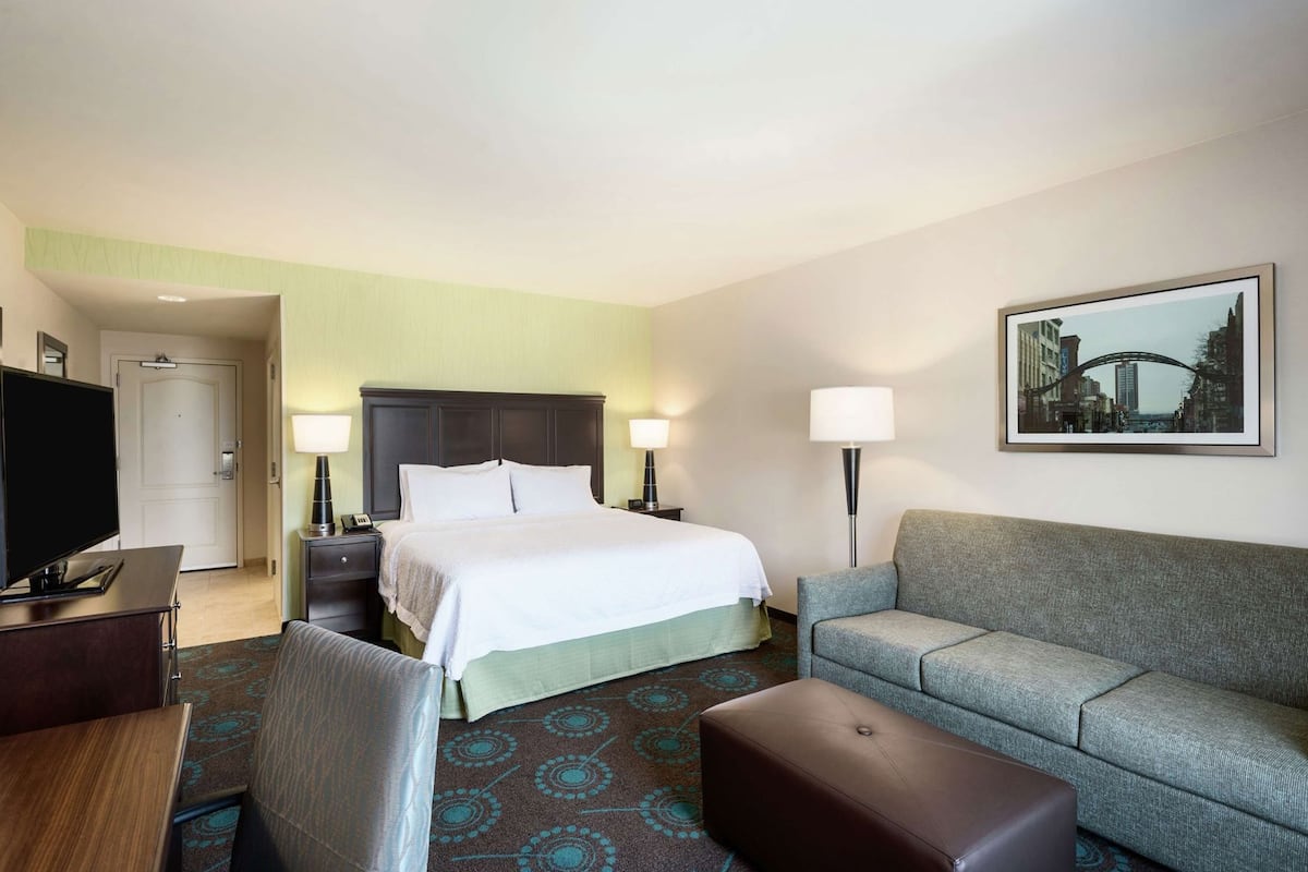A hotel room with a bed, a sofa, a TV, and a framed picture on the wall.