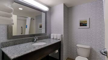 Un baño con lavamanos de granito, un espejo, un inodoro y papel tapiz estampado.