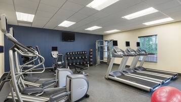 A fitness center with treadmills, elliptical machines, and a wall of dumbbells.