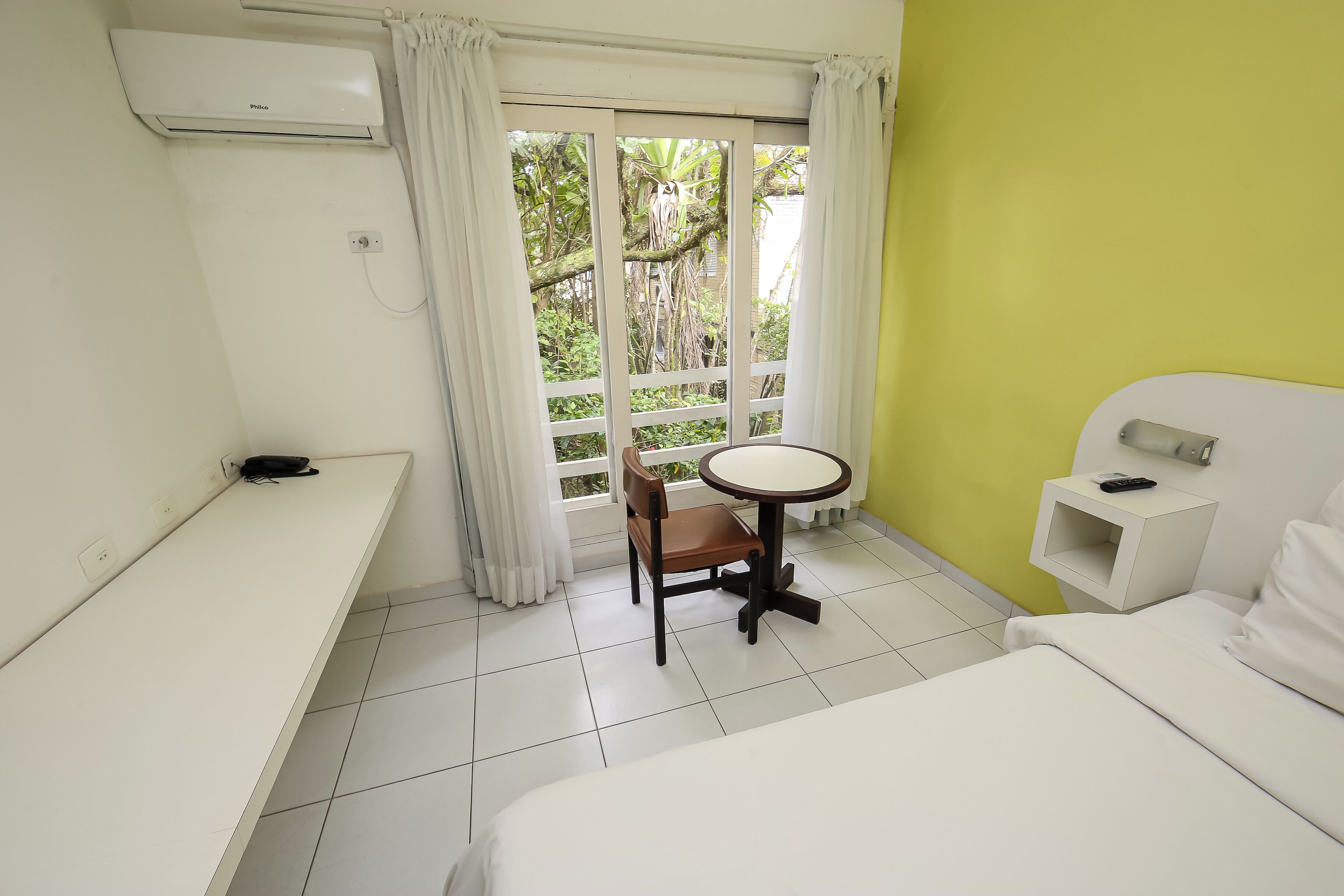 Ein Hotelzimmer mit einem Bett, einem kleinen runden Tisch mit Stuhl, einem Schreibtisch und einem Fenster mit Vorhängen.