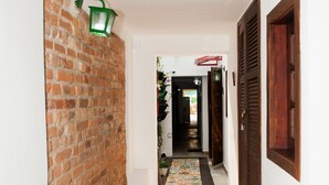 Un pasillo estrecho con una pared de ladrillo en un lado, una puerta de madera en el otro y un accesorio de luz verde fijado a la pared.