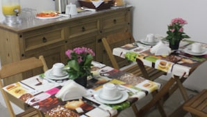 Un comedor con una mesa larga preparada para el desayuno, sillas de madera, una cafetera y una cesta de frutas.