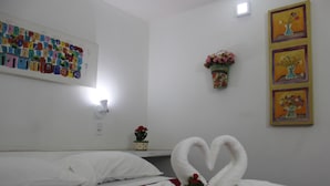 Habitación de hotel con cama, una obra de arte en la pared, una planta pequeña en maceta y una decoración con forma de corazón en una toalla.