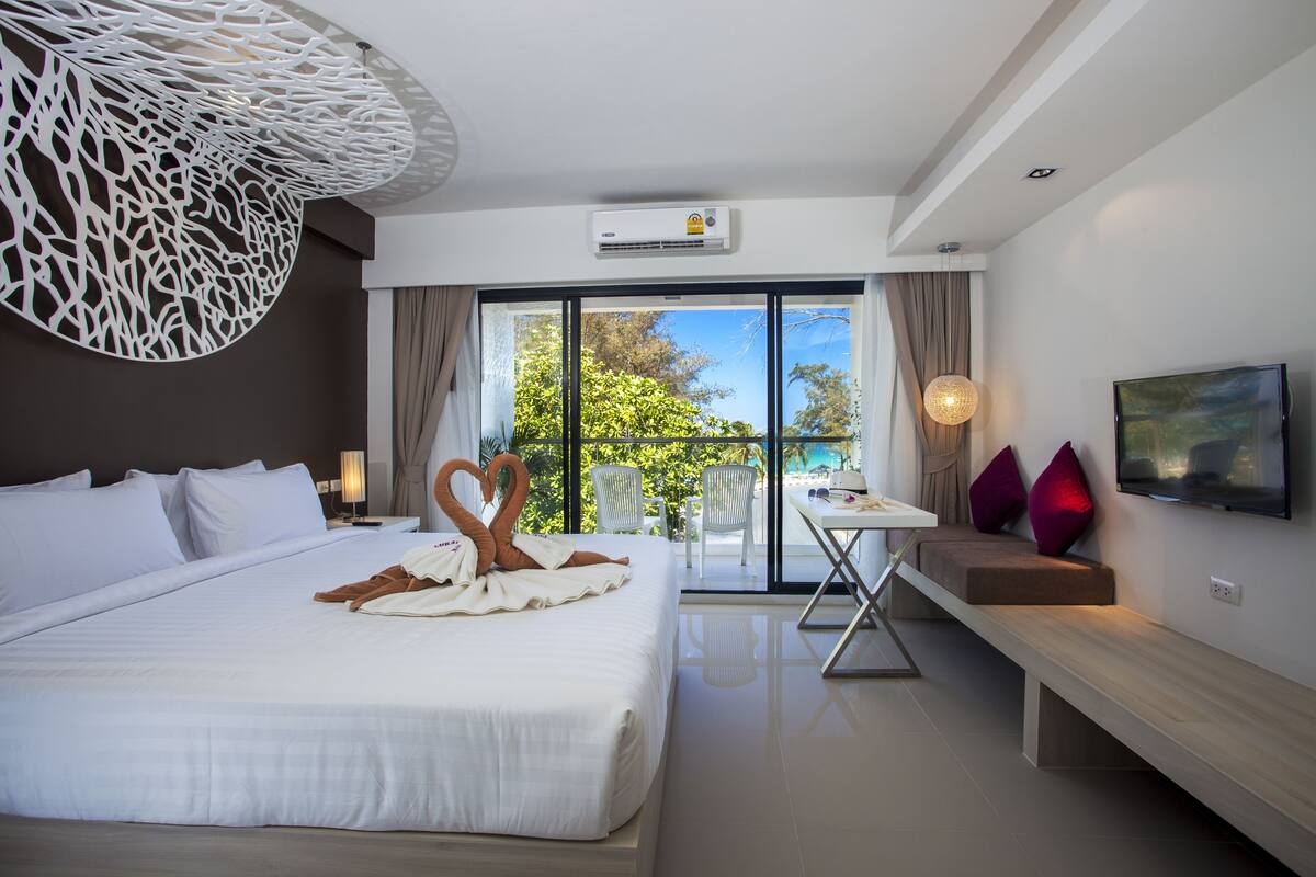Una habitación de hotel moderna con una cama grande, un balcón con mesa y sillas, televisión y un diseño de techo original.