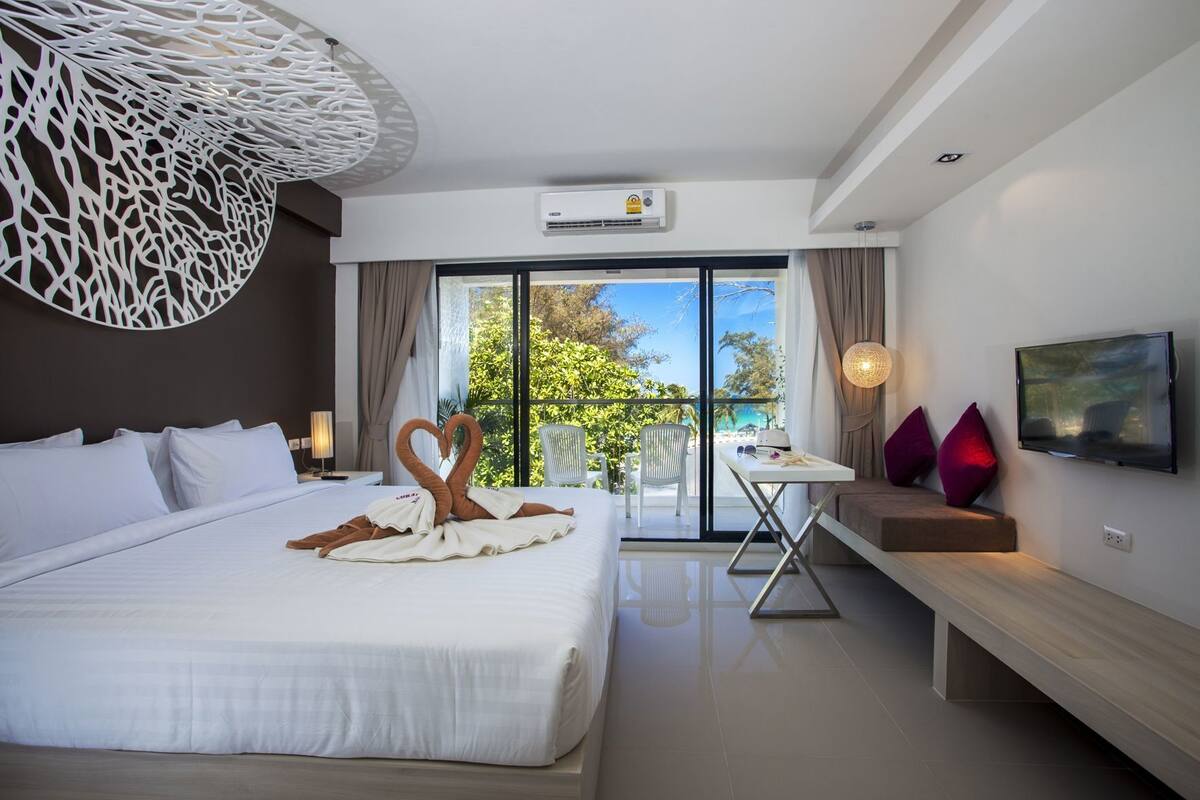 Habitación de hotel moderna con una cama grande, un balcón con vistas, televisión y zona de comedor.