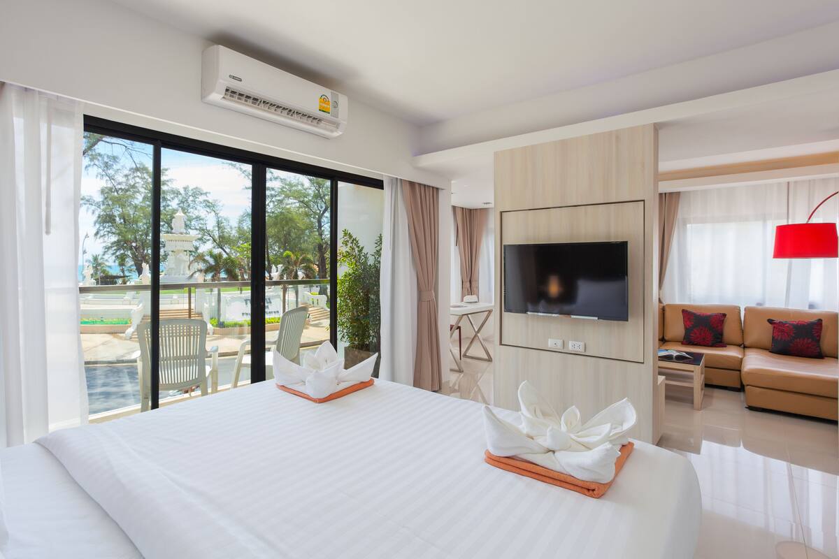 Una habitación de hotel con una cama grande, televisión, sofá y balcón con mobiliario exterior.