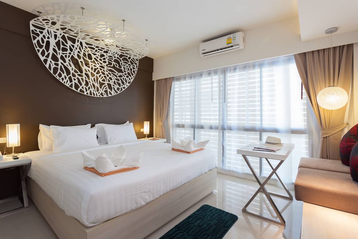 Habitación de hotel con una cama grande, mesitas de noche, un escritorio y vistas al exterior a través de amplias ventanas.