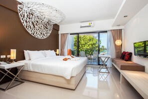 A modern hotel room with a large bed, a balcony with a table and chairs, and a TV mounted on the wall. - Coral Inn (Karon)