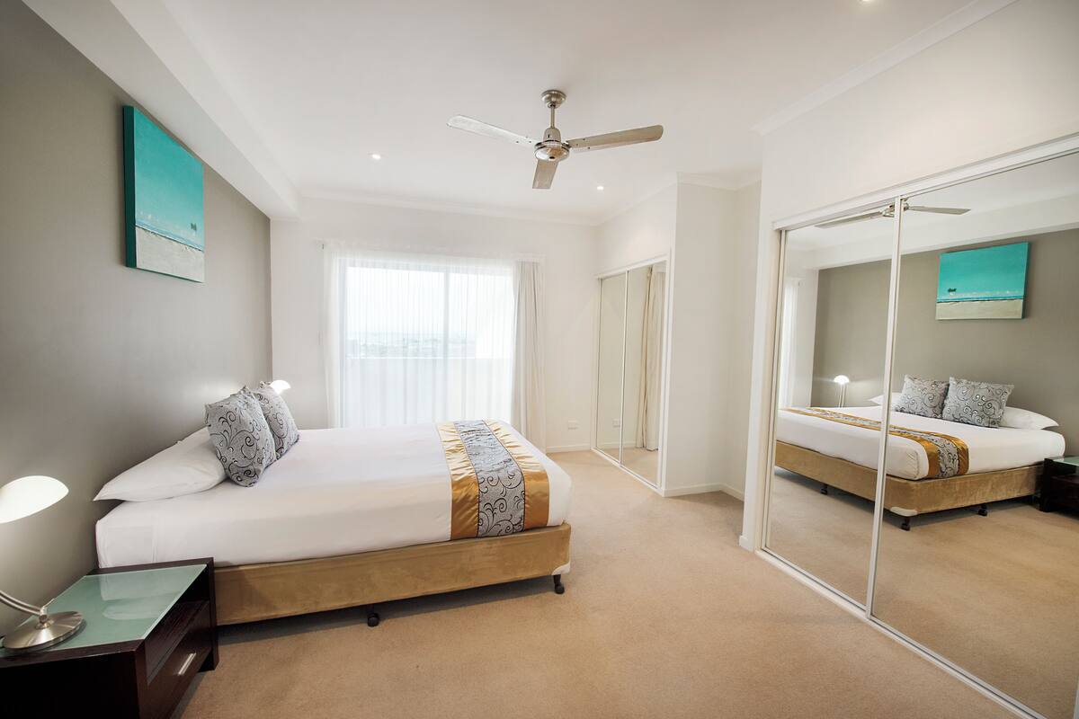A bedroom with a bed, bedside table, mirror, and ceiling fan.