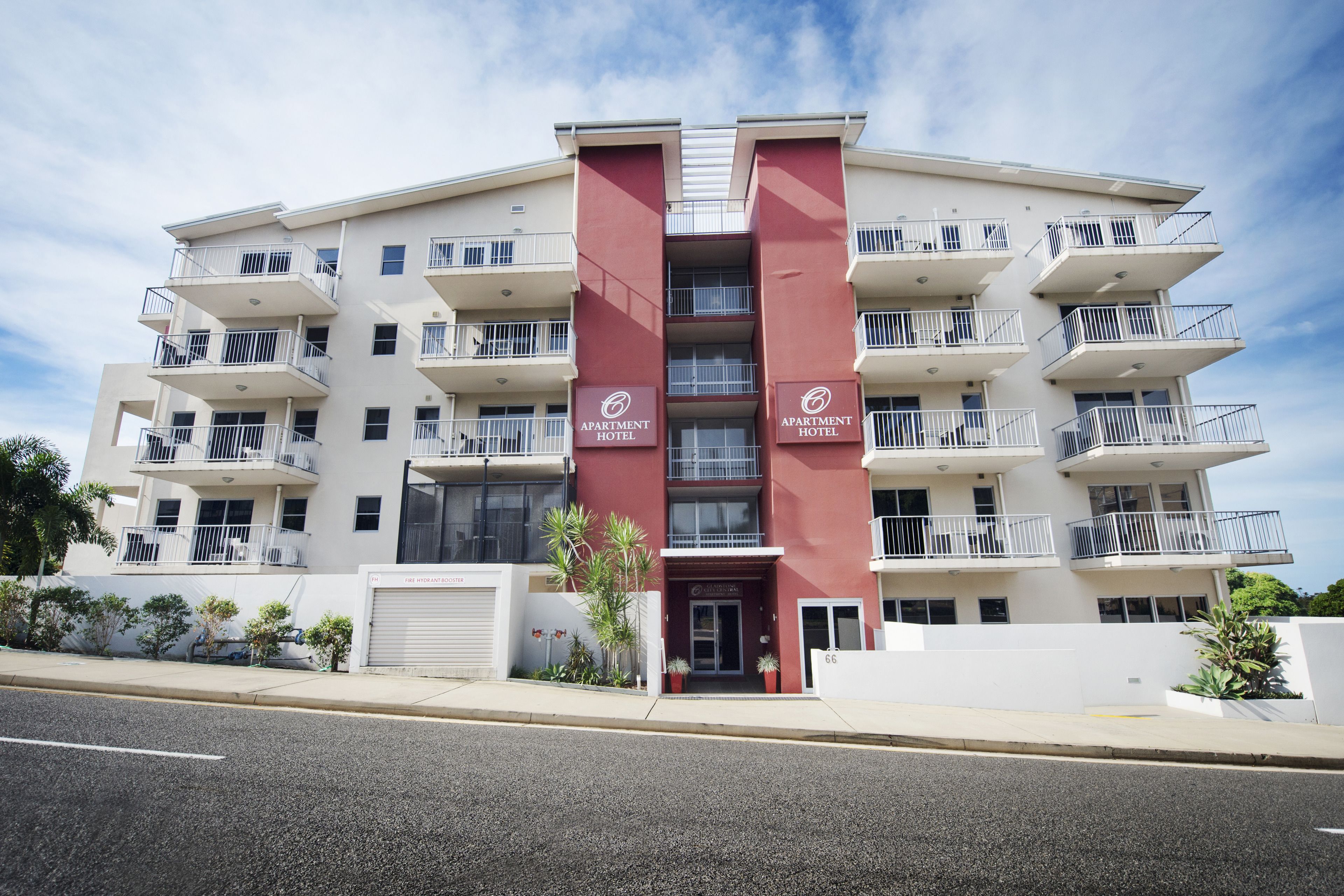 Un hotel-apartamento de varios pisos, con balcones, una entrada principal y un estacionamiento.