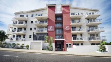 Un hotel-apartamento de varios pisos, con balcones, una entrada principal y un estacionamiento.