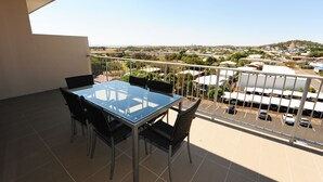 A balcony with a glass table and chairs, offering a view of a parking area and buildings in the distance. - Gladstone City Central Apartment Hotel (Gladstone)