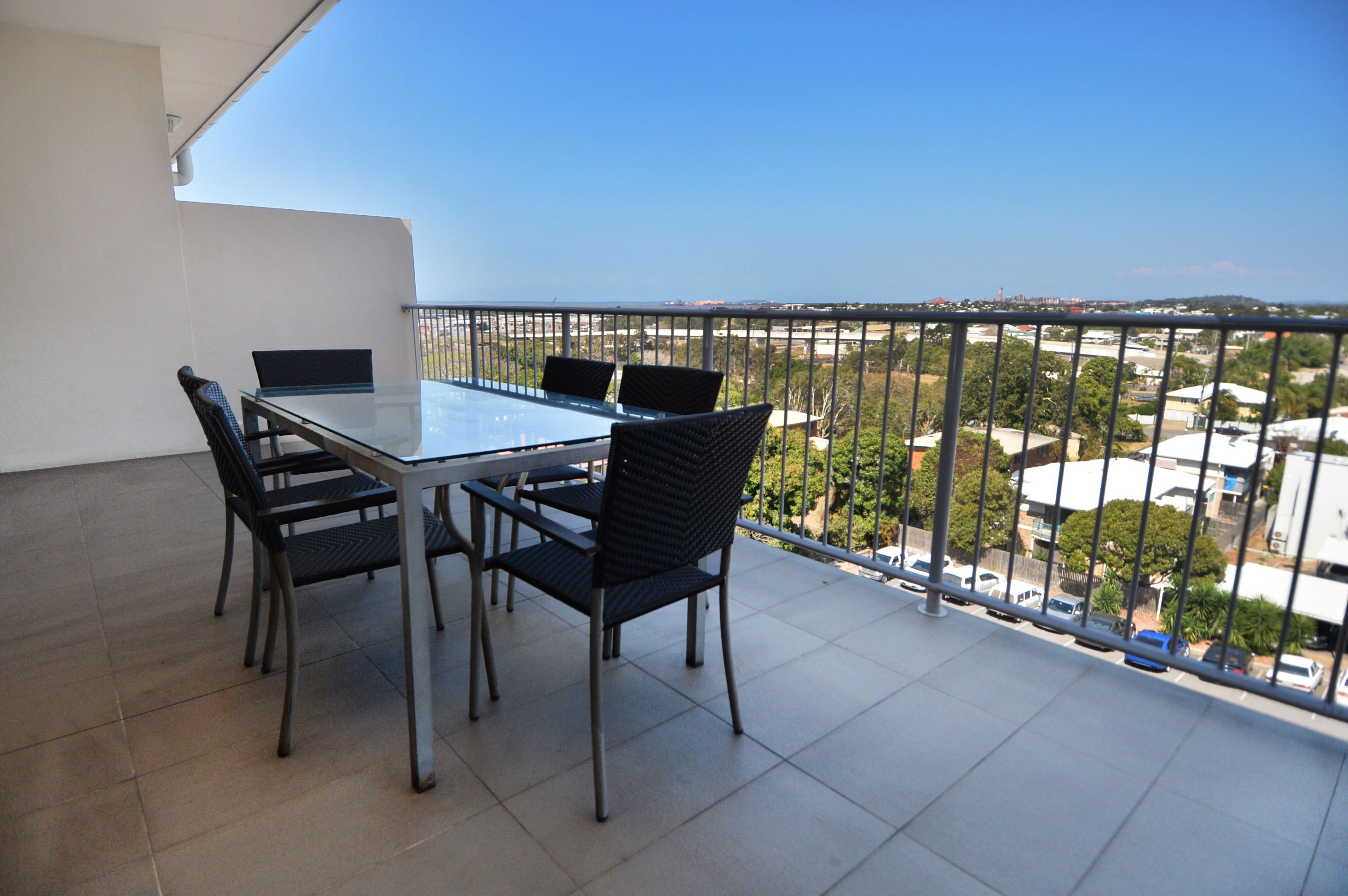 A balcony with a glass table and four chairs, offering a view of a cityscape.