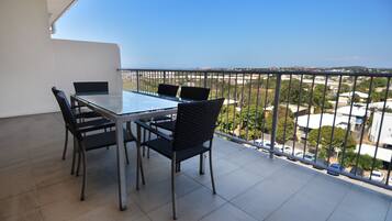 A balcony with a glass table and four chairs, offering a view of a cityscape.