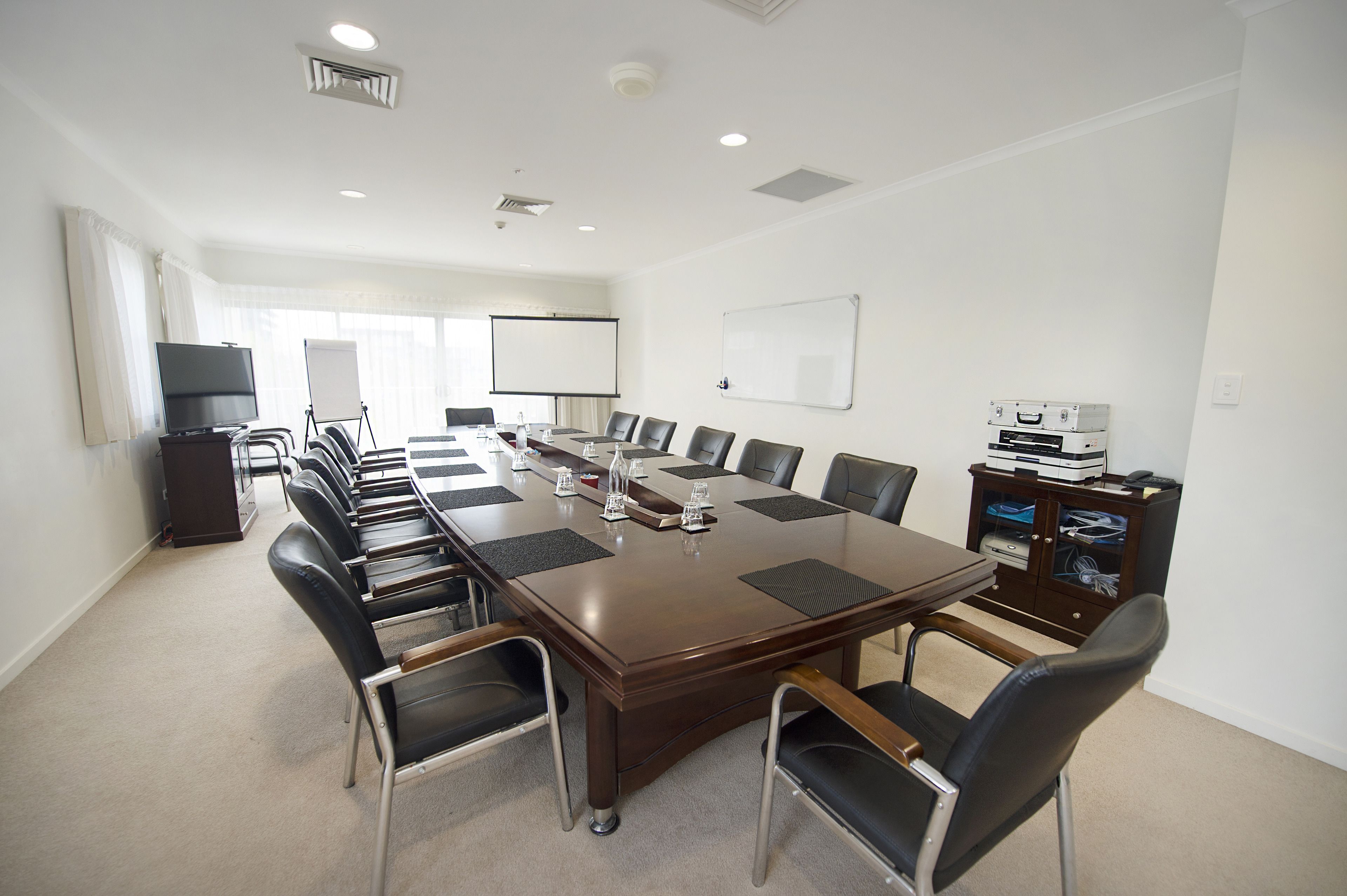 A conference room with a long table, chairs, a projector screen, and a whiteboard.