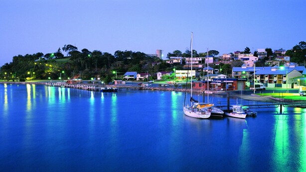 A waterfront marina with boats docked, a pier extending into the water, and buildings with illuminated windows. - Gladstone City Central Apartment Hotel (Gladstone)