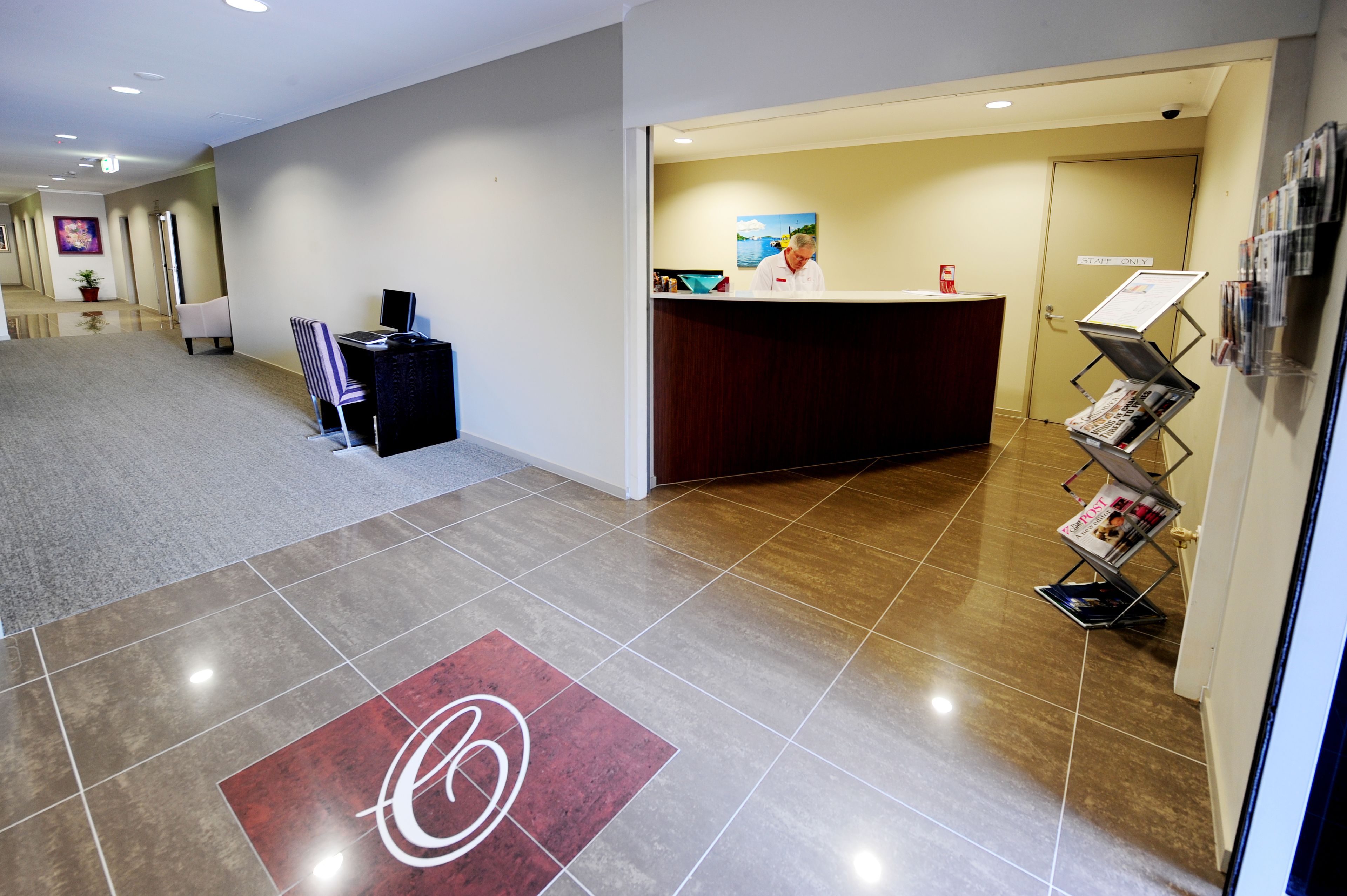Un espace d’accueil d’hôtel comprenant un comptoir de réception, un espace d’attente avec des chaises et un panneau d’affichage avec des magazines.