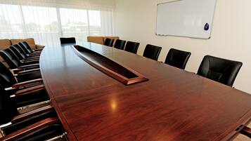 A conference room with a long wooden table, black chairs, a whiteboard, and a view through large windows.
