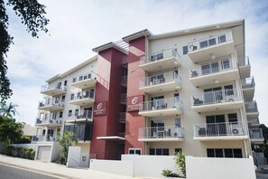 Un edificio de apartamentos de varios pisos con balcones, un pilar central rojo y un letrero que indica que es un hotel-apartamento.