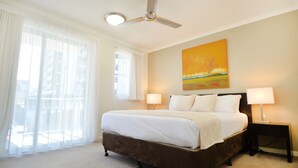 A hotel room with a large bed, two bedside lamps, a ceiling fan, and a painting on the wall. - Gladstone City Central Apartment Hotel (Gladstone)