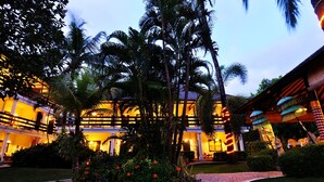 Un hotel a più piani con facciata luminosa, palme e un vialetto lastricato.