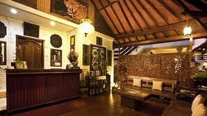 Un'area reception con scrivania in legno, una zona salotto con divano e poltrone, e una parete decorativa con motivi elaborati.