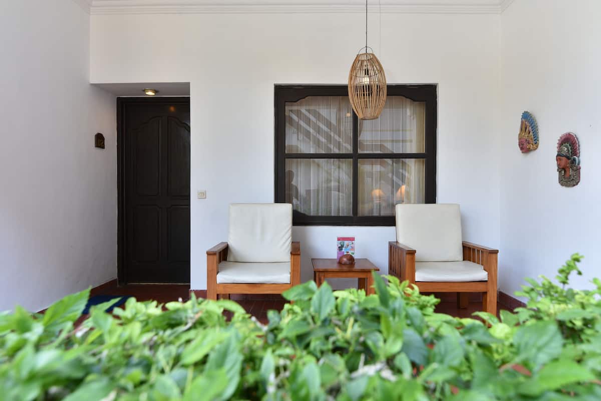 A room with two wooden chairs, a small table, a window with curtains, and decorative wall art.