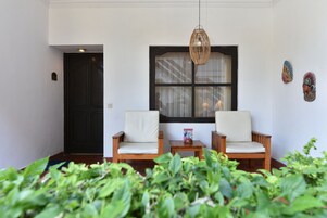 Una habitación con dos sillas de madera, una mesa pequeña, una ventana con cortinas y decoración en la pared.