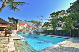 Una piscina con borde de baldosas, sillas de descanso y una palmera.