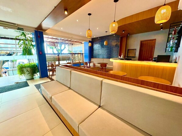 A modern hotel lobby with a reception desk, seating area, and a large potted plant. - Hit Hotel (Salvador)