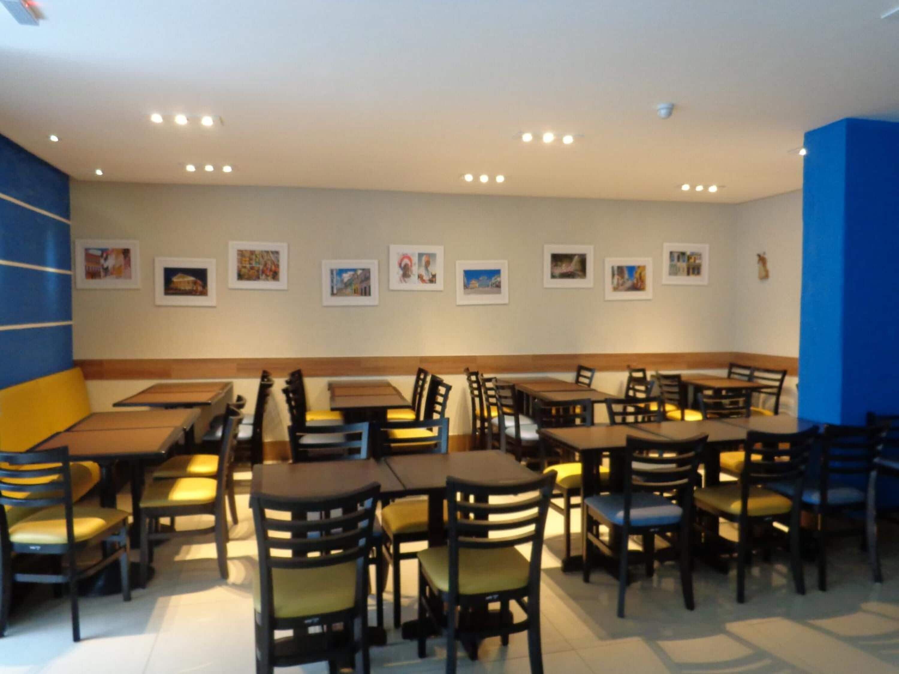 Un restaurant doté de nombreuses tables et chaises, d’un plafond haut avec des luminaires encastrés et de tableaux encadrés aux murs.
