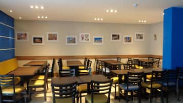 Un restaurant doté de nombreuses tables et chaises, d’un plafond haut avec des luminaires encastrés et de tableaux encadrés aux murs.