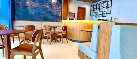 A modern hotel lobby with a curved reception desk, wooden chairs, a blue cushioned seating area, and pendant lighting.