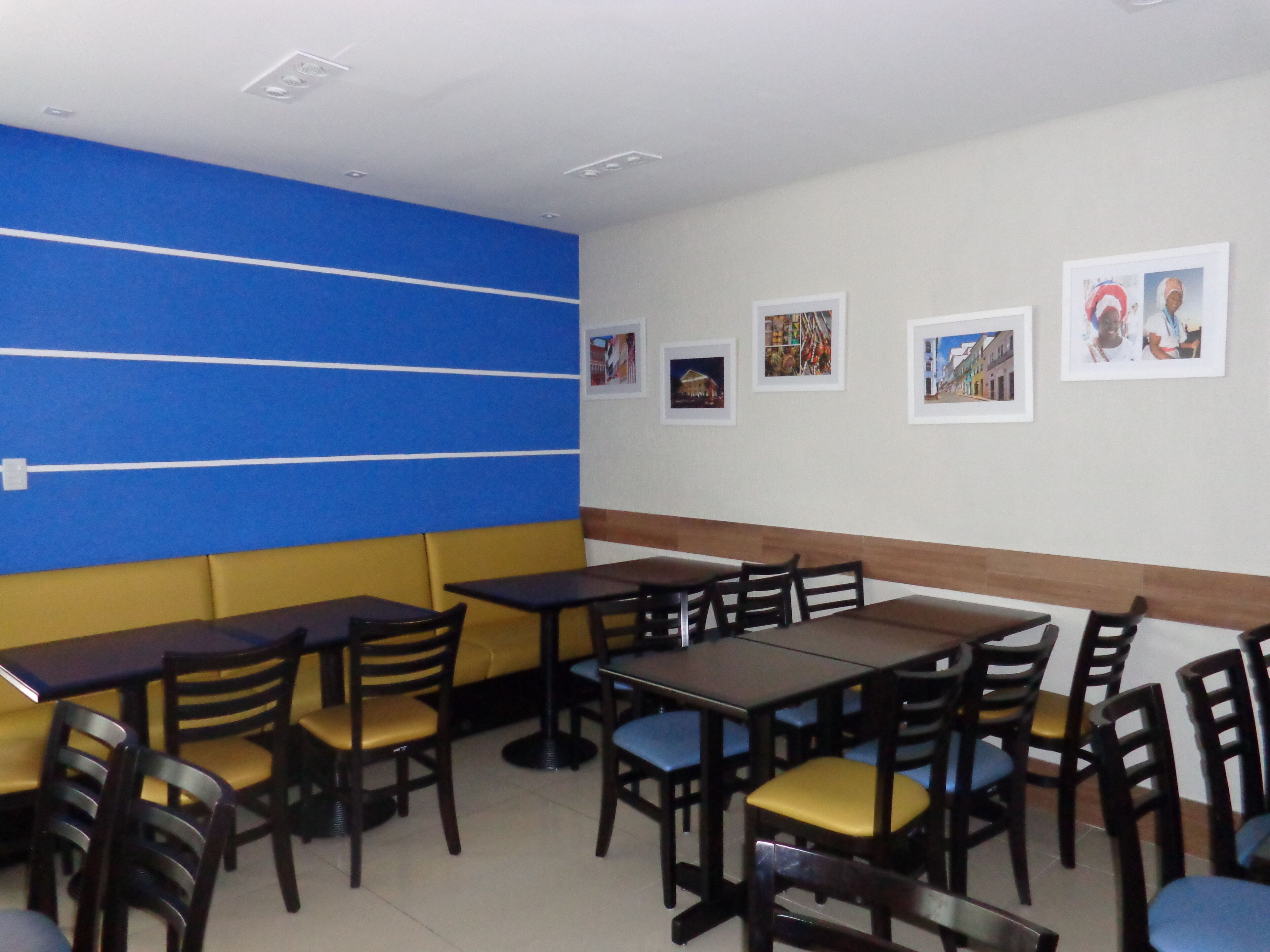 Een restaurant met zitjes en tafels, blauwgele wanden en ingelijste foto’s aan de muur.