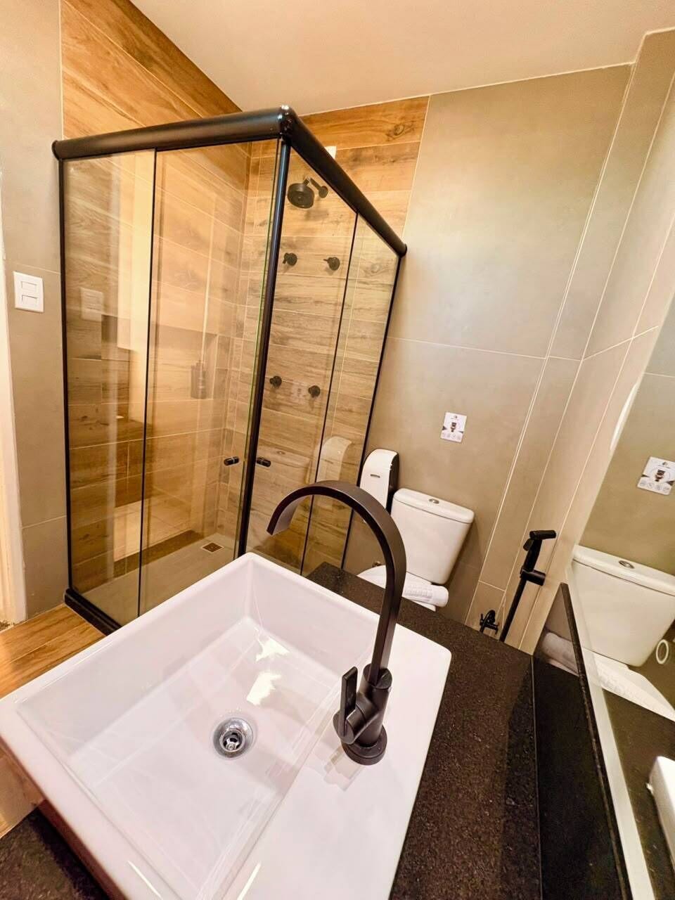 Un baño con cabina de ducha de vidrio, un lavabo blanco con grifo moderno y un inodoro.