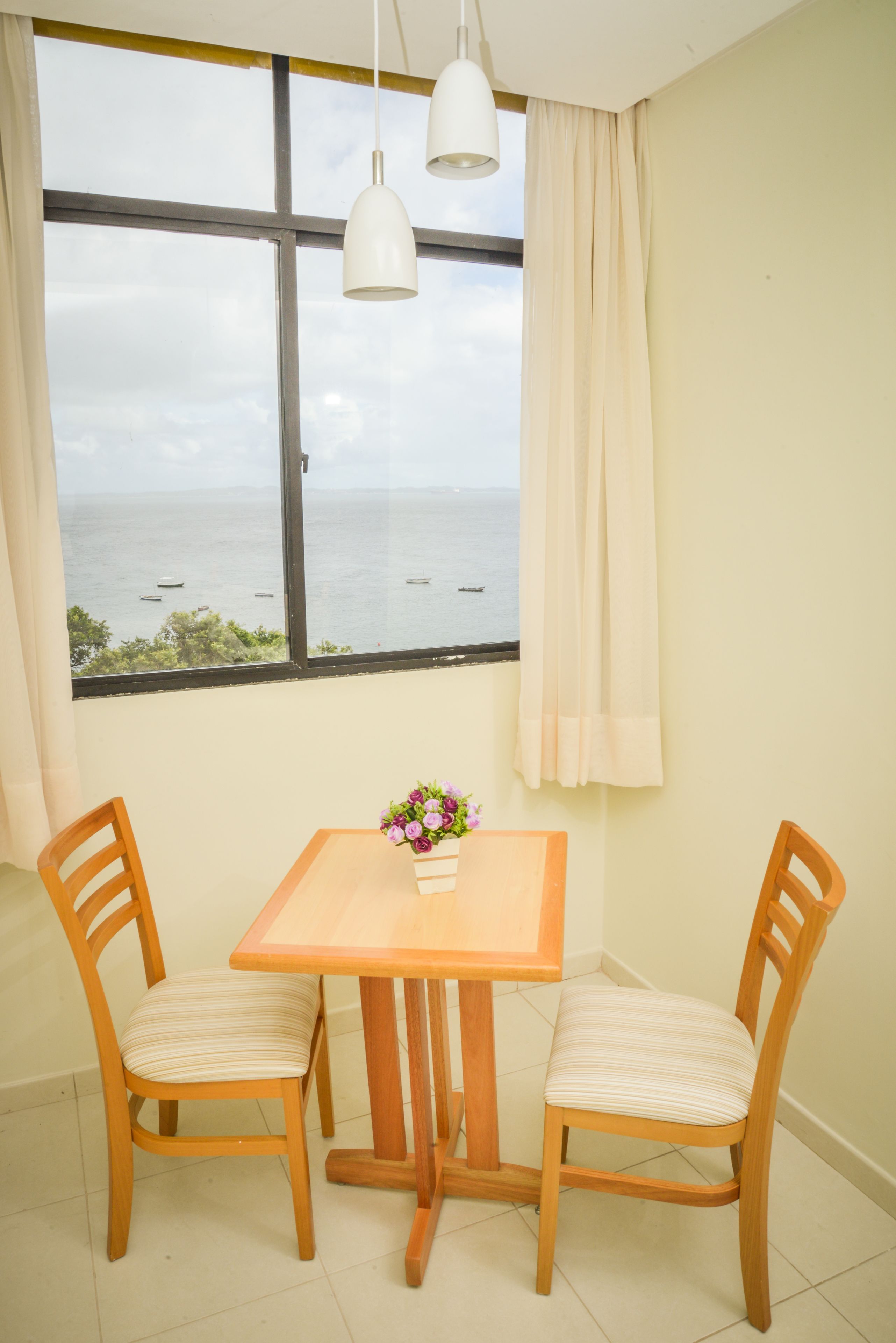 Una habitación con un ventanal amplio, una mesa de madera con dos sillas y un florero con flores.