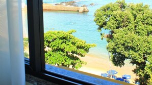 Vista di una spiaggia attraverso una finestra, con il mare, una spiaggia sabbiosa e un po' di vegetazione.