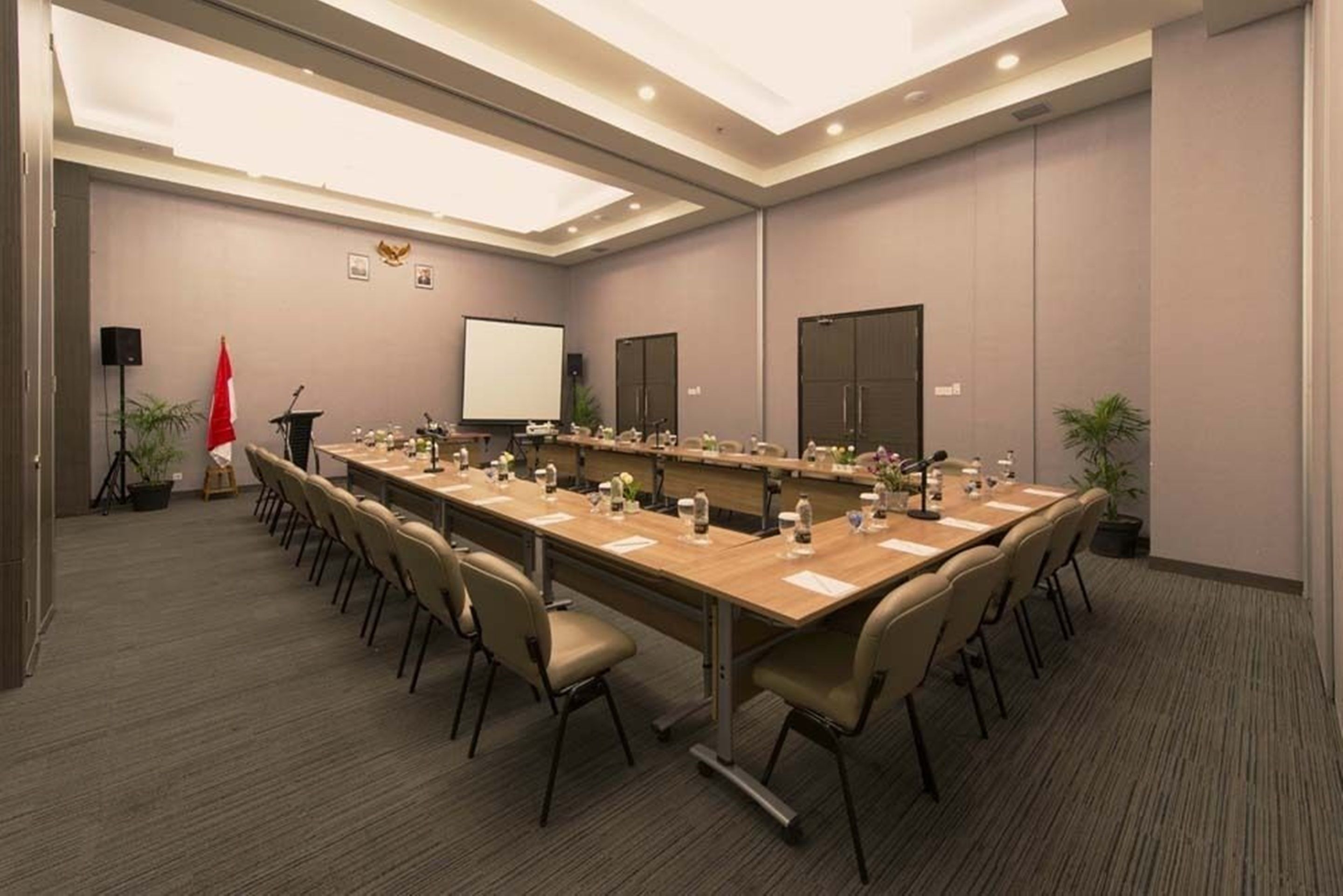 Un salón de conferencias con una larga mesa, sillas, una pantalla de proyector y un atril.