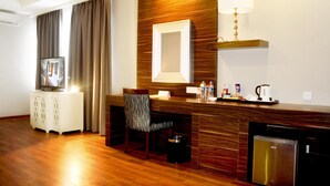 Une chambre d’hôtel avec un plancher en bois, un bureau avec une chaise, une télévision, un minibar, une lampe et une machine à café.