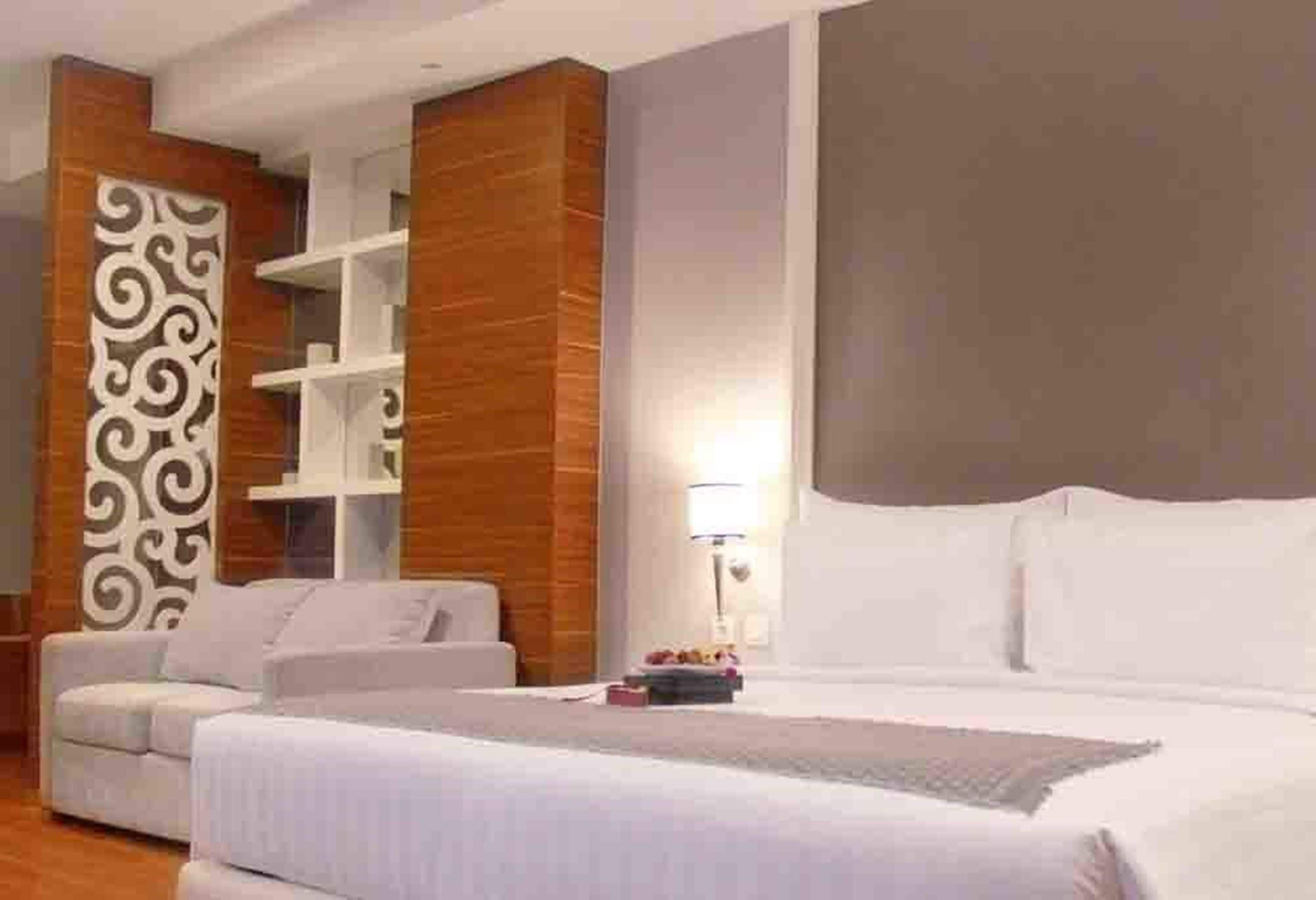 Une chambre d’hôtel moderne dotée d’un grand lit, d’un canapé, d’un panneau mural décoratif et d’étagères intégrées.