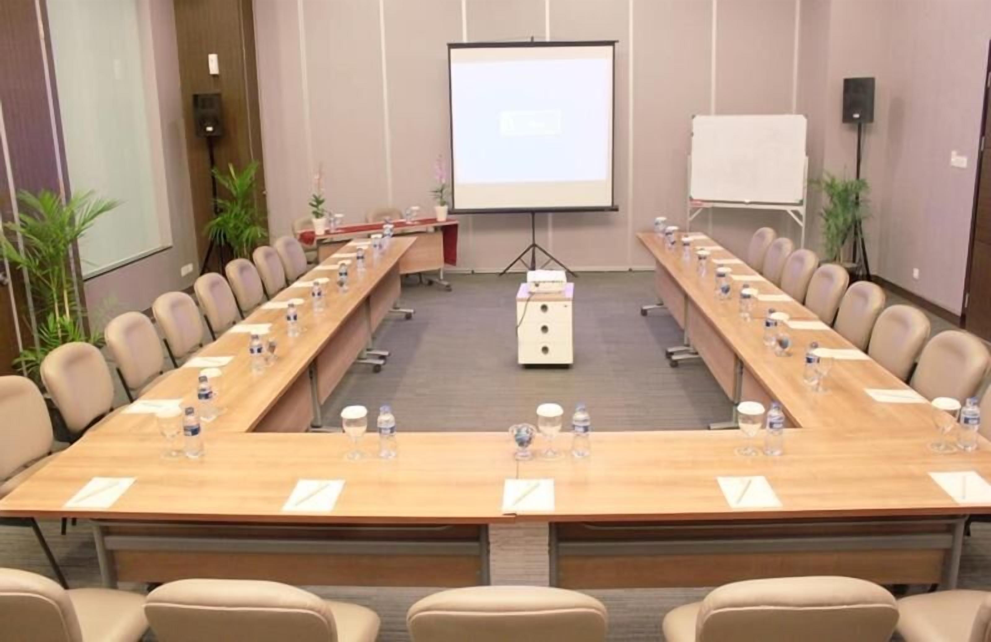 Un salón de conferencias con una larga mesa, sillas, una pantalla de proyector y una pizarra.