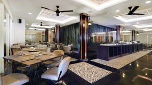 Un restaurant moderne doté de nombreuses tables et chaises, d’un bar central et de ventilateurs de plafond.