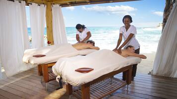 A massage parlor with wooden floors and white curtains, overlooking a beach.