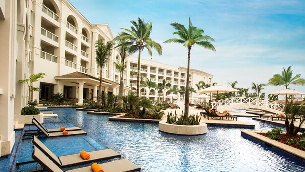 Zona de piscina de hotel con sillones de descanso y palmeras.