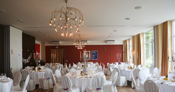 A banquet hall with round tables, white tablecloths, and chairs with white covers and purple bows.