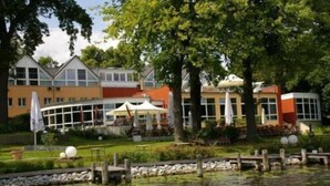 A lakeside hotel with a restaurant patio, outdoor seating, and a stone dock. - DämeritzSeehotel (Berlin)