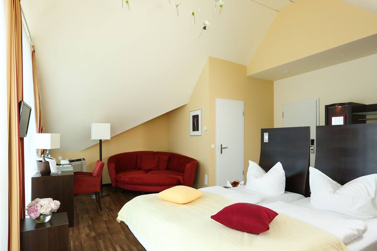 A hotel room with a bed, a red sofa, a desk with a computer, and a door.