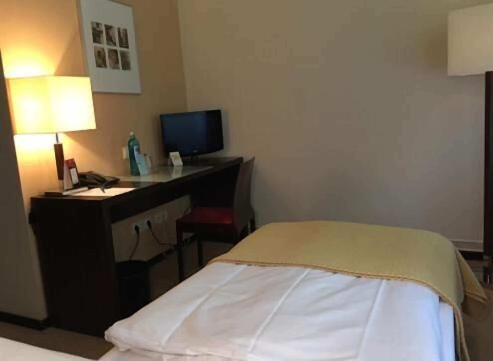 A hotel room with a bed, a desk with a computer, a lamp, and a television.