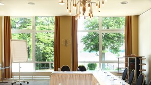 A conference room with a long table, chairs, a whiteboard, and large windows with a view of trees. - DämeritzSeehotel (Berlin)
