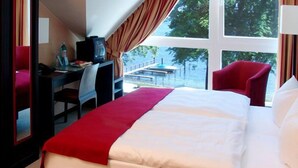 A hotel room with a bed, a desk, a chair, and a window with a view of trees. - DämeritzSeehotel (Berlin)